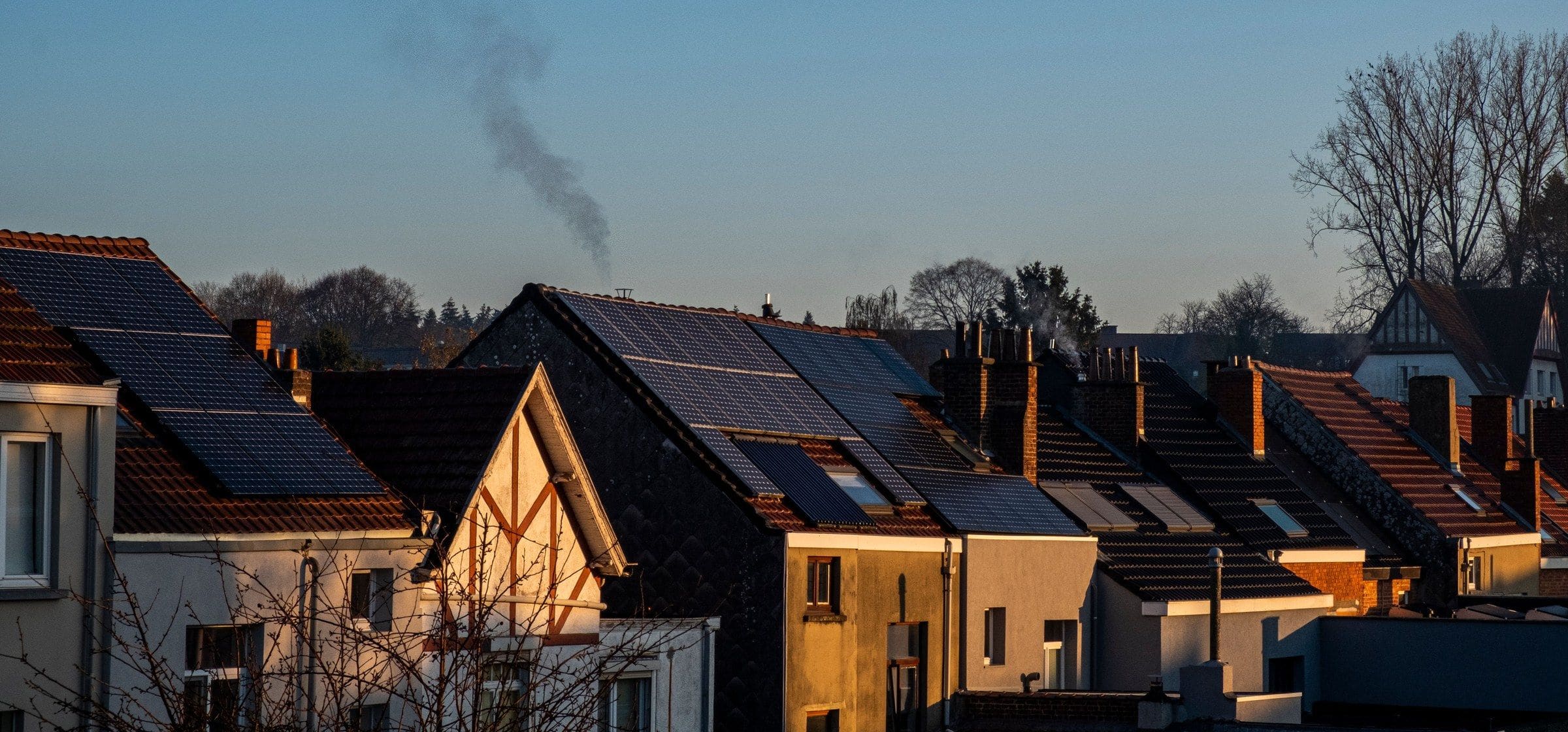 Rooftops carrying solar panels in low evening sun, chimney smoke rising